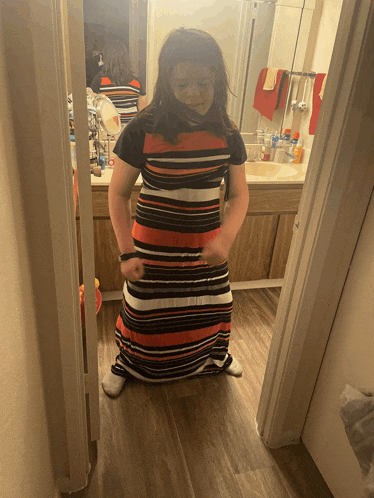 a girl in a striped dress is kneeling in front of a bathroom mirror