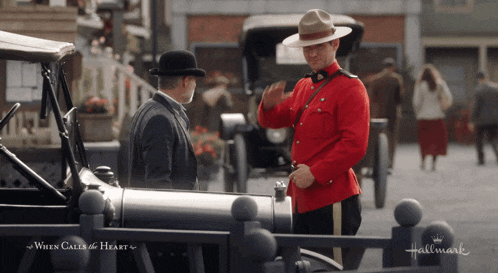 a man in a red uniform is talking to a man in a hat in a hallmark movie