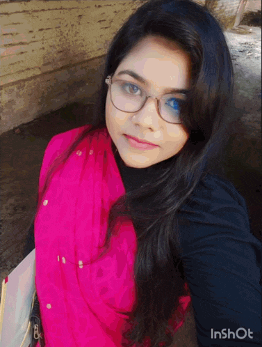 a woman wearing glasses and a pink scarf is taking a selfie with inshot