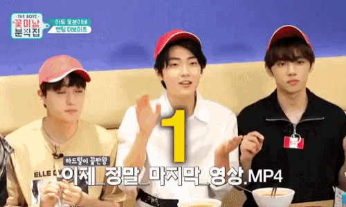 a group of young men are sitting at a table eating food and one of them is wearing a number 1 hat .