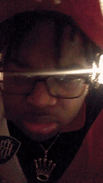 a person wearing glasses and a necklace with a crown on it