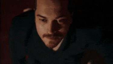 a close up of a man 's face with a mustache in a dark room .