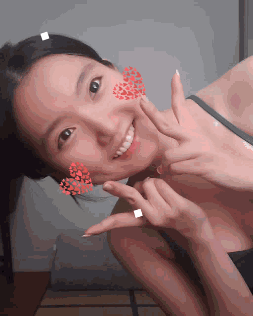 a woman with hearts on her cheeks is smiling and making a peace sign