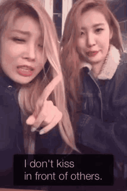 two women are standing next to each other and one of them is pointing at the camera with the words i don 't kiss in front of others