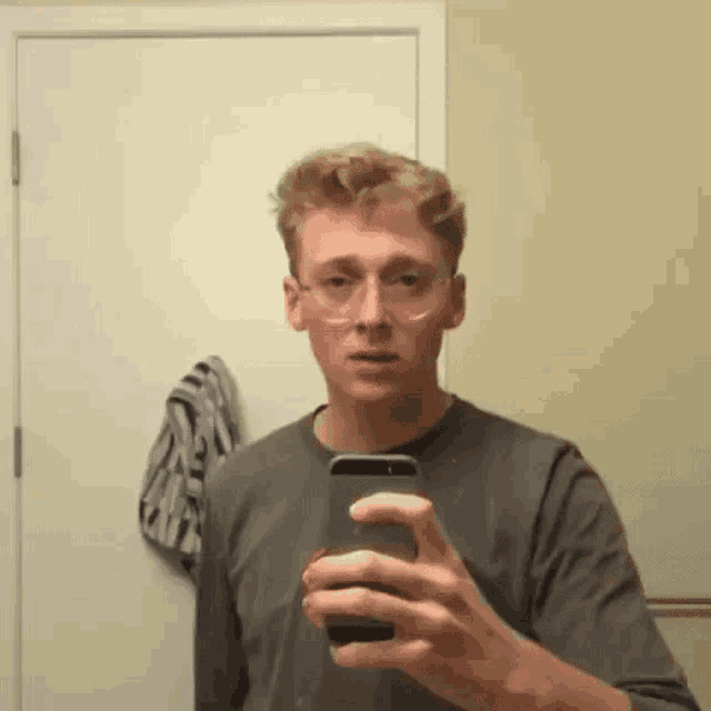 a young man wearing glasses is taking a selfie in a bathroom mirror .