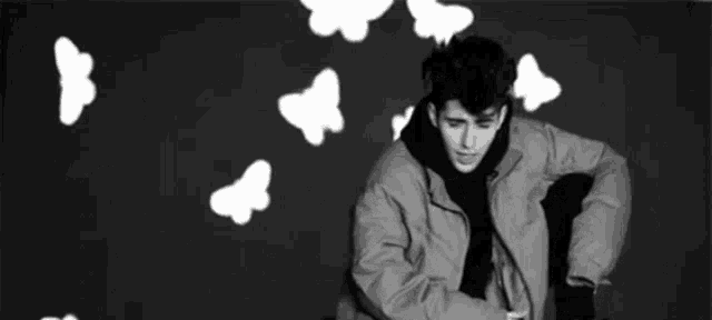a black and white photo of a young man with butterflies flying around him