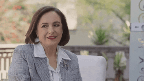 a woman is sitting in a chair wearing a suit and pearls and smiling .