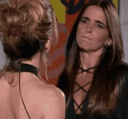 two women are standing next to each other and talking to each other in front of a painting .