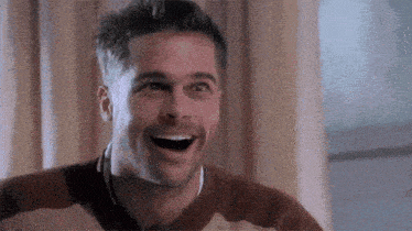 a man is laughing with his mouth open while wearing a brown and white sweater .