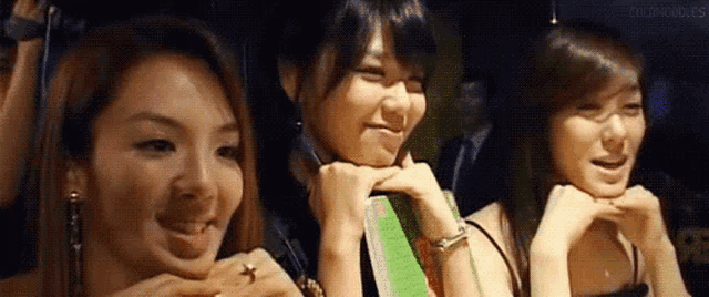 three women are sitting next to each other with their hands on their chins .