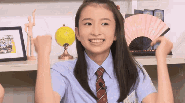 a girl in a blue shirt and red tie is holding a fan