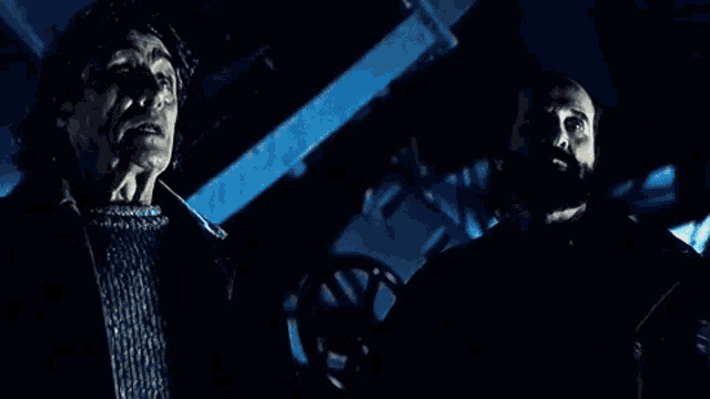 two men are standing next to each other in a dark room in a movie scene .