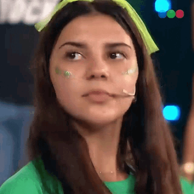 a woman wearing a green shirt and a green headband has green paint on her face