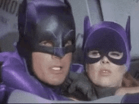 a man and a woman in purple batman costumes are sitting next to each other .