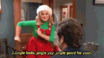 a woman in an elf costume sings jingle bells to a man