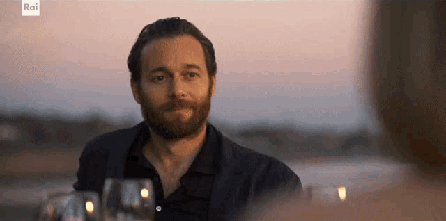 a man with a beard is sitting at a table with glasses of wine and a sign that says rai on the bottom