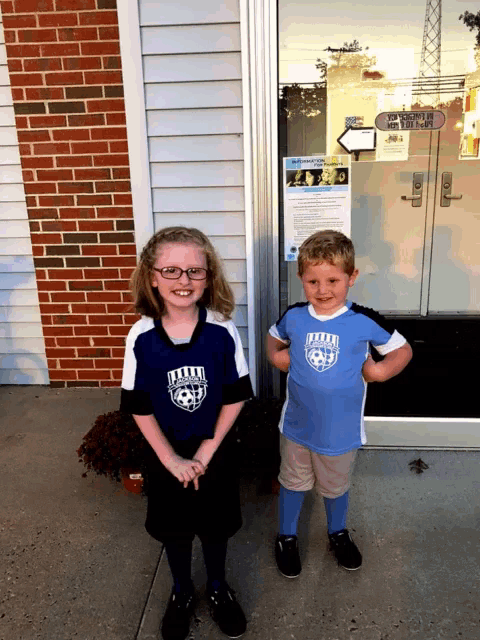 a boy and a girl are standing in front of a brick building wearing jerseys that say little league