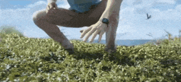 a man wearing a smart watch is squatting on a grassy field .