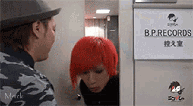 a man in a hat stands next to a woman with red hair in a b.p. records room