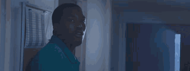 a man in a blue shirt is standing in a hallway with a bulletin board in the background