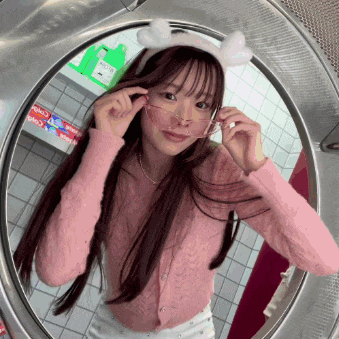 a girl wearing a pink sweater and bunny ears adjusts her glasses in a washing machine