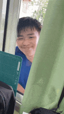 a young man looks out of a window with a green cutting board behind him