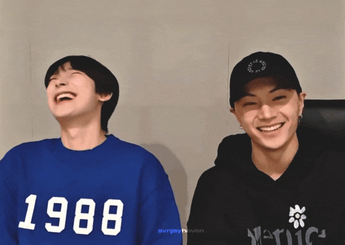 two young men are laughing and one of them is wearing a 1988 sweatshirt