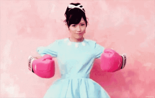 a woman in a blue dress is wearing pink boxing gloves against a pink background .