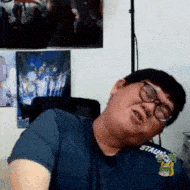 a man wearing glasses and a blue shirt is making a funny face while sitting in a chair .
