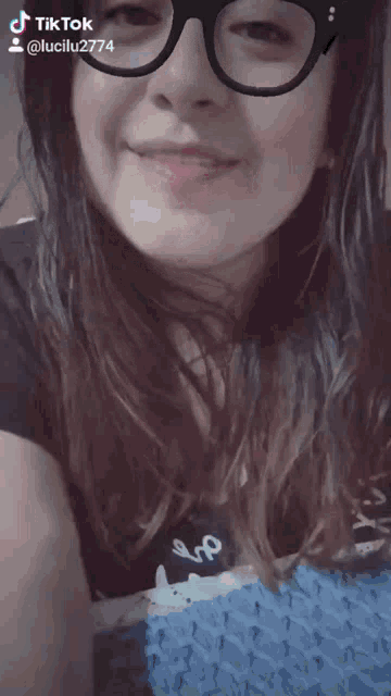 a woman wearing glasses and a black shirt is smiling for a tiktok video