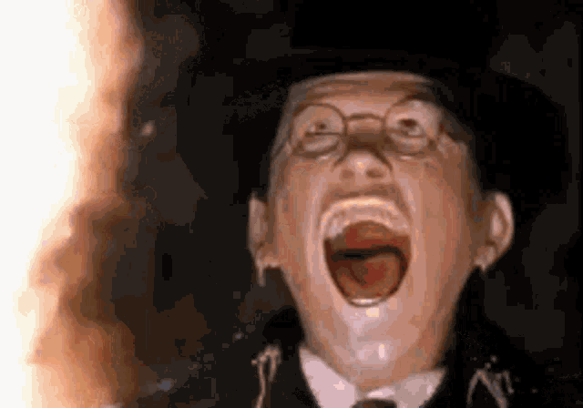 a man in a top hat and glasses is screaming with his mouth open .