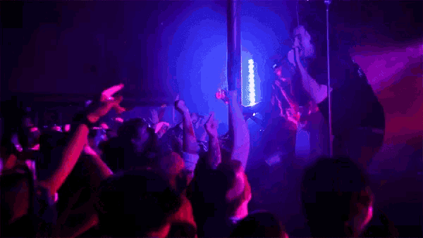 a man singing into a microphone in front of a crowd of people with their hands in the air