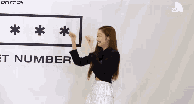a woman in a black crop top and silver skirt is standing in front of a sign that says `` t number '' .