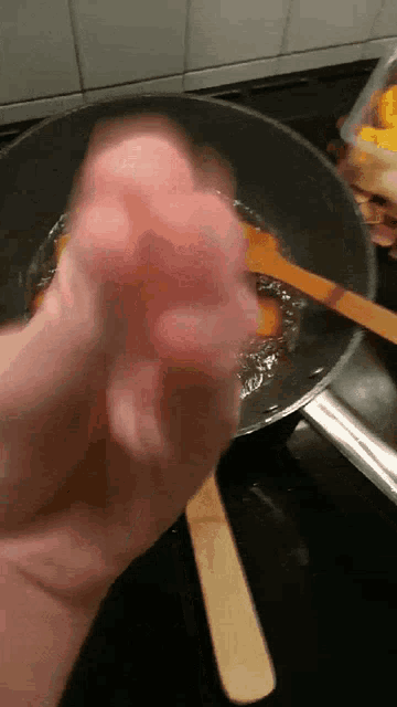 a person 's hand is holding a wooden spoon over a frying pan