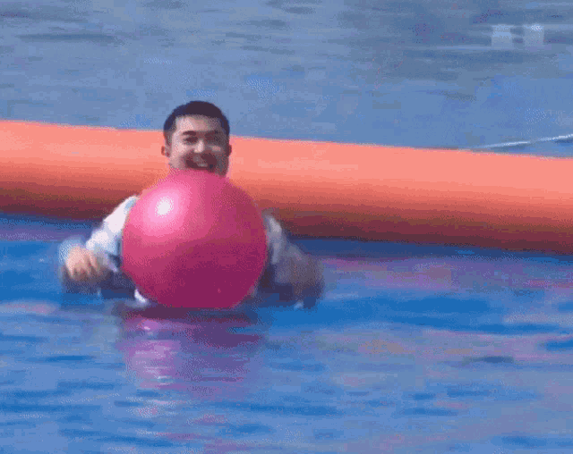 a man is holding a pink ball in a pool with chinese writing