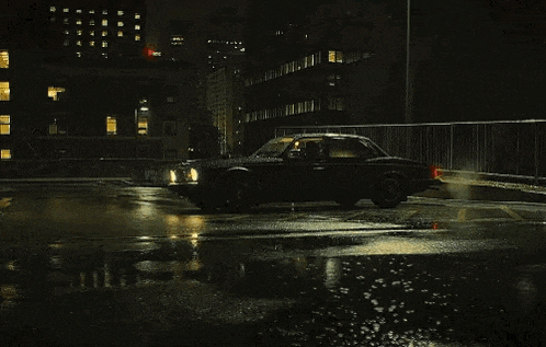 a black car is driving on a wet street at night .