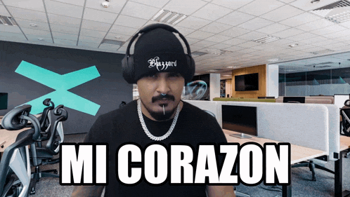 a man wearing headphones and a beanie says mi corazon in an office