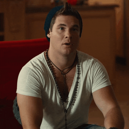 a man wearing a white t-shirt and a beanie is sitting on a red couch