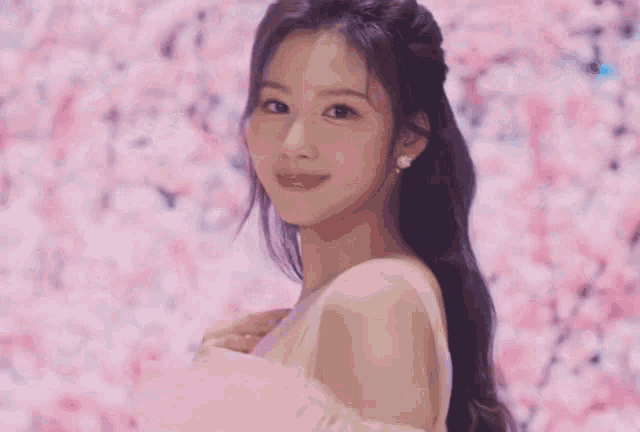 a woman in a pink dress is standing in front of a wall of flowers .