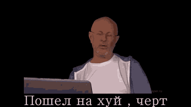 a man with glasses and a beard is looking at a laptop screen with the words " пошел на хуй " on the bottom