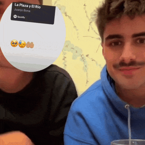 two men sitting next to each other with a sticker that says la plaza y el rio juanjo bona