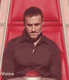 a man in a black shirt is sitting in a red chair with his eyes closed .