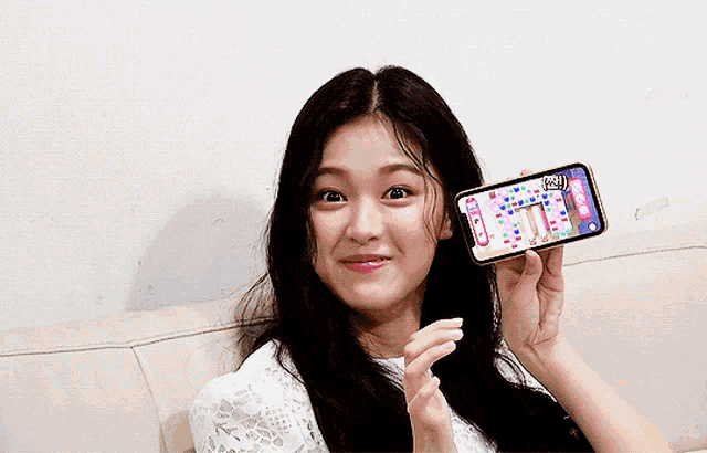 a woman holds up a cell phone with a game on the screen