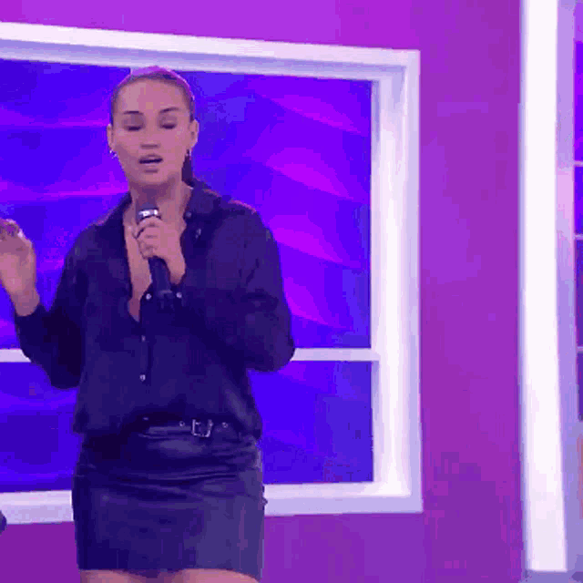 a woman singing into a microphone in front of a purple background