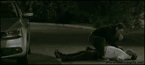 a man is laying on the ground next to a car while another man tries to help him .