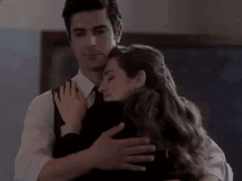 a man in a suit and tie is hugging a woman in a black shirt