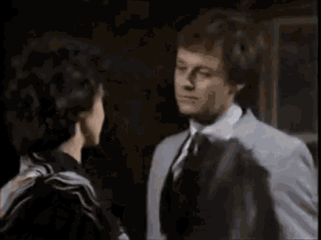 a man in a suit and tie is talking to a woman in a black dress .