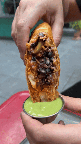 a person is holding a burrito in their hands and dipping it in green sauce