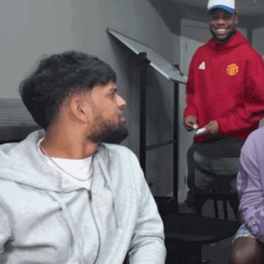 a man in a red manchester united sweatshirt smiles at another man