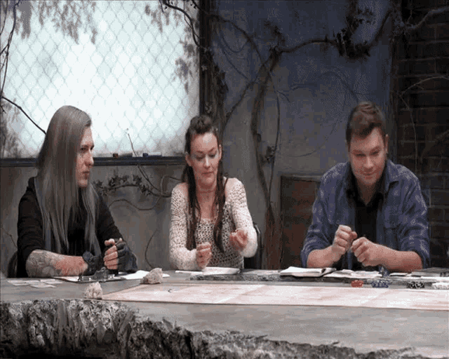 three people are sitting at a table playing a game with dice